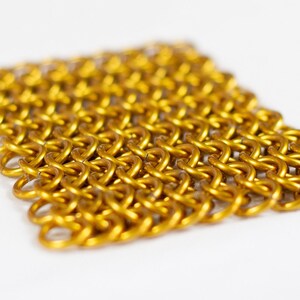 Puede incluir: Un primer plano de una malla de cota de malla dorada, un tipo de armadura de metal tejido.