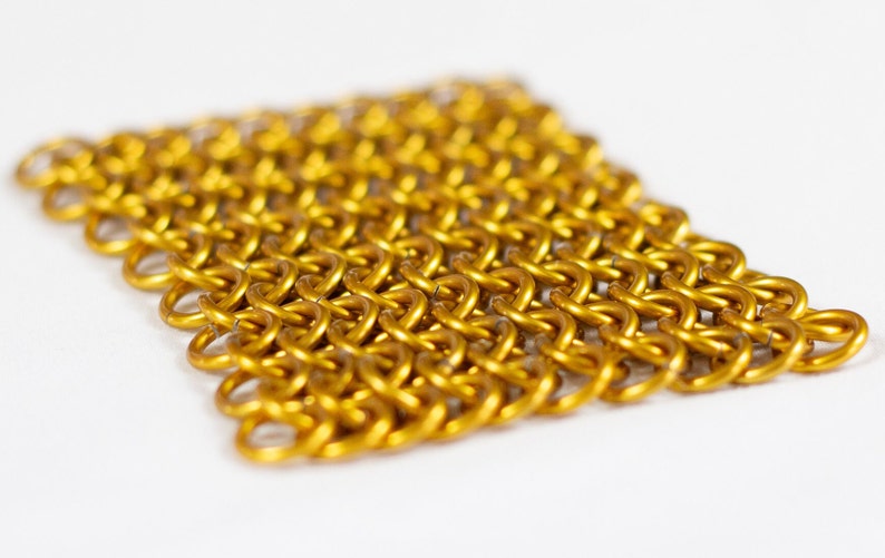 Puede incluir: Un primer plano de una malla de cota de malla dorada, un tipo de armadura de metal tejido.