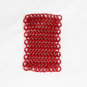 Puede incluir: Una malla de cota de malla roja, hecha de peque&ntilde;os anillos de metal interconectados. La malla es plana y de forma rectangular.