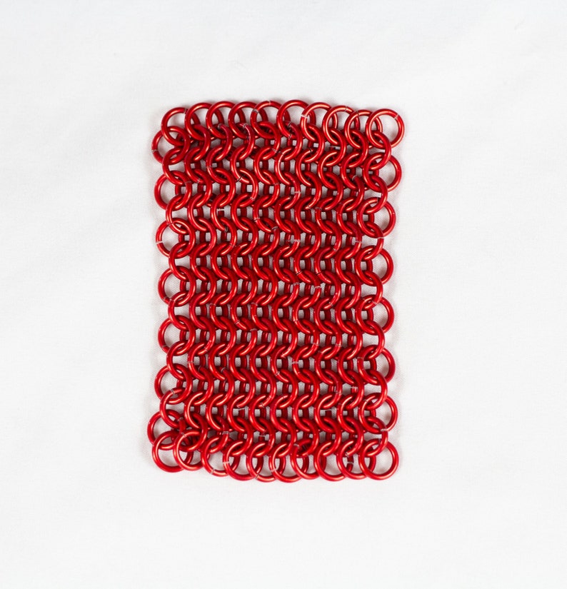 Puede incluir: Una malla de cota de malla roja, hecha de peque&ntilde;os anillos de metal interconectados. La malla es plana y de forma rectangular.