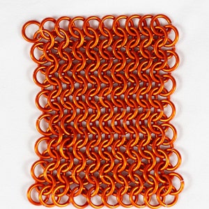 Puede incluir: Un primer plano de un trozo cuadrado de cota de malla naranja. La cota de malla est&aacute; hecha de peque&ntilde;os anillos de metal interconectados.