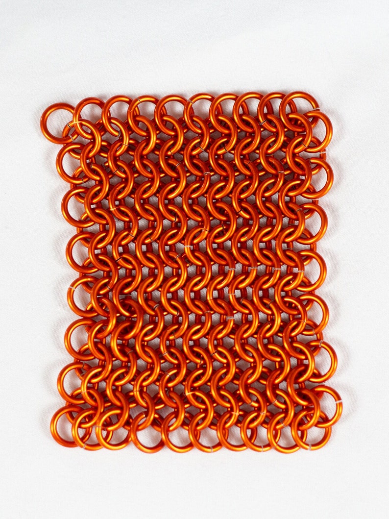 Puede incluir: Un primer plano de un trozo cuadrado de cota de malla naranja. La cota de malla est&aacute; hecha de peque&ntilde;os anillos de metal interconectados.