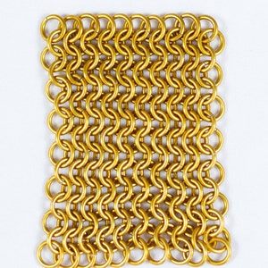Puede incluir: Un cuadrado de cota de malla dorada, hecho de anillos de metal entrelazados. La cota de malla es un tipo de malla met&aacute;lica tejida.