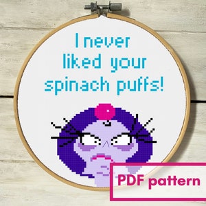 Peut inclure: Un motif de point de croix dans un cercle à broder en bois. Le motif présente un personnage de dessin animé pixélisé avec des cheveux violets et une expression de colère. Le texte "I never liked your spinach puffs!" est au-dessus du personnage. Le texte "PDF pattern" est dans un encadré rose.