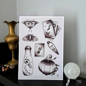 May include: A black and white illustration print featuring a variety of spooky and mystical imagery, including a pumpkin, a crystal, a bottle with a skull inside, a moth, and tarot cards. The print is on white paper and has a black border.