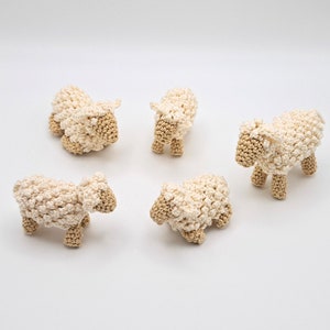 Könnte beinhalten: Fünf gehäkelte weiße Schafe mit braunen Gesichtern. Die Schafe stehen auf einer weißen Oberfläche.