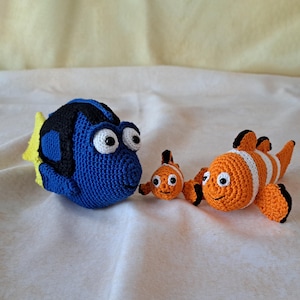 Può includere: Tre giocattoli di peluche a forma di pesce all'uncinetto. Un pesce Dory blu e nero, un pesce pagliaccio arancione e bianco e un pesce pagliaccio arancione e bianco più piccolo.