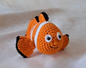 May include: A crocheted orange and white clownfish toy with black eyes and a smiling mouth.