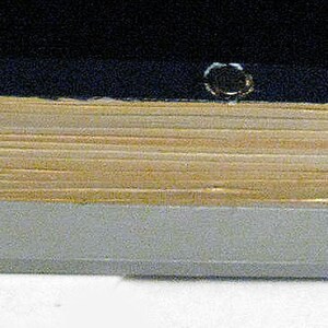 K&ouml;nnte beinhalten: Nahaufnahme der Unterkante eines Buches mit schwarzem Einband, goldfarbenem R&uuml;cken und grauem Sockel.