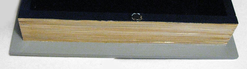 K&ouml;nnte beinhalten: Nahaufnahme der Unterkante eines Buches mit schwarzem Einband, goldfarbenem R&uuml;cken und grauem Sockel.