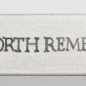 K&ouml;nnte beinhalten: Eine wei&szlig;e Holzkiste mit den Worten "The North Remembers" auf der Vorderseite eingraviert. Die Kiste hat ein silbernes Schwert und einen silbernen Pfeil mit einem blauen Edelstein an jedem Ende.