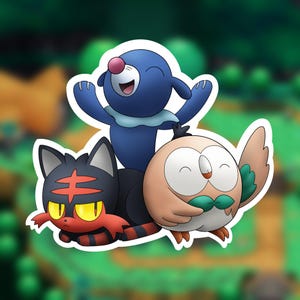 May include: A sticker featuring three cartoon creatures: a blue seal-like character with a pink nose, a black and red cat-like character with yellow eyes, and a round tan owl-like character with green accents, all arranged in a group.