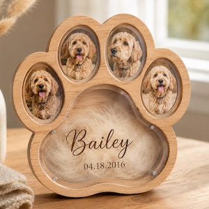 May include: A light-coloured wooden paw-shaped photo frame featuring three oval openings for dog portraits. The central section contains a patch of light-coloured fur behind glass, with the name Bailey and the date 04.18.2016 printed in dark script.