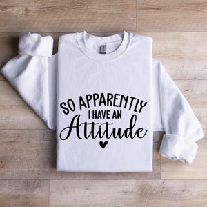 K&ouml;nnte beinhalten: Wei&szlig;es Langarmshirt mit schwarzem Text, der "So Apparently I Have An Attitude" mit einem kleinen Herzsymbol lautet.