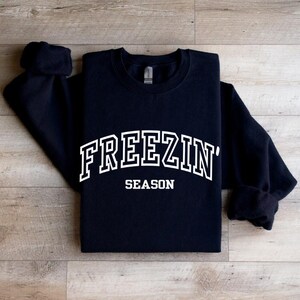 Może przedstawiać: Czarna bluza z białym napisem "FREEZIN' SEASON".