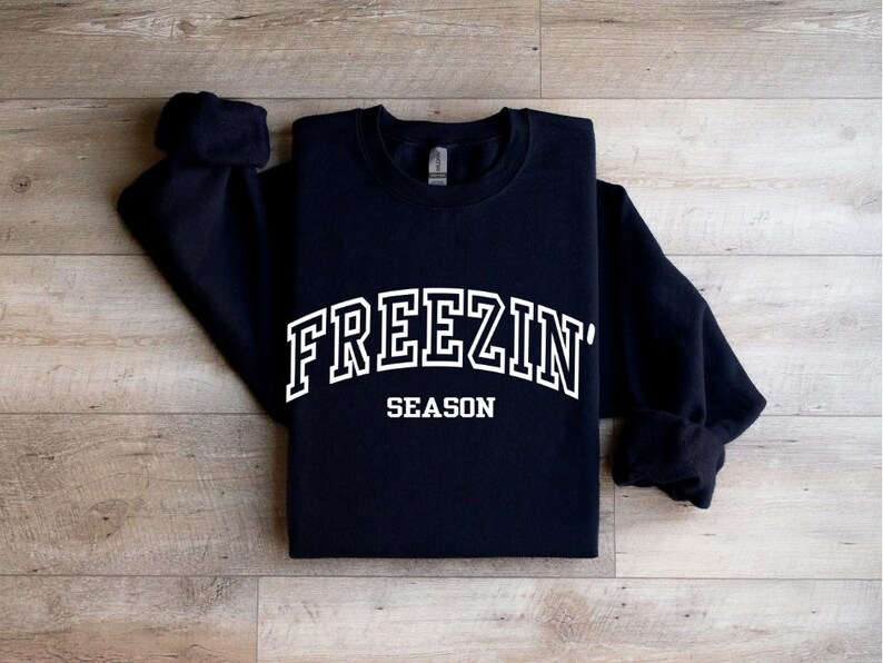 Może przedstawiać: Czarna bluza z białym napisem "FREEZIN' SEASON".