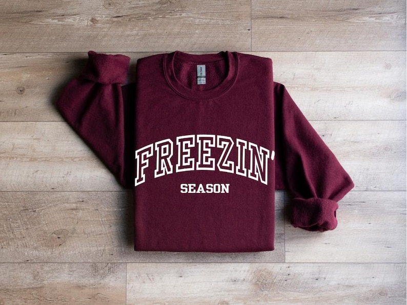 Może przedstawiać: Bordowy longsleeve z białym napisem "FREEZIN' SEASON"