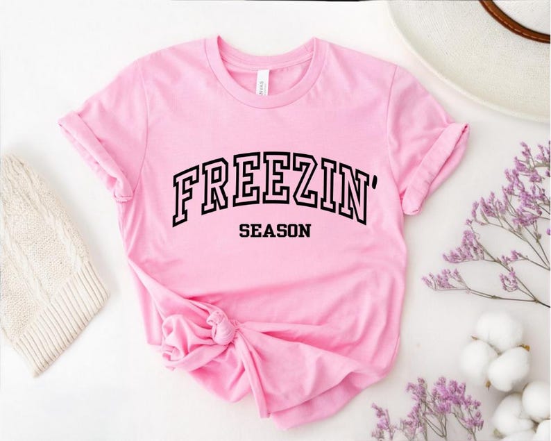Może przedstawiać: R&oacute;żowa koszulka z czarnym napisem "FREEZIN' SEASON"