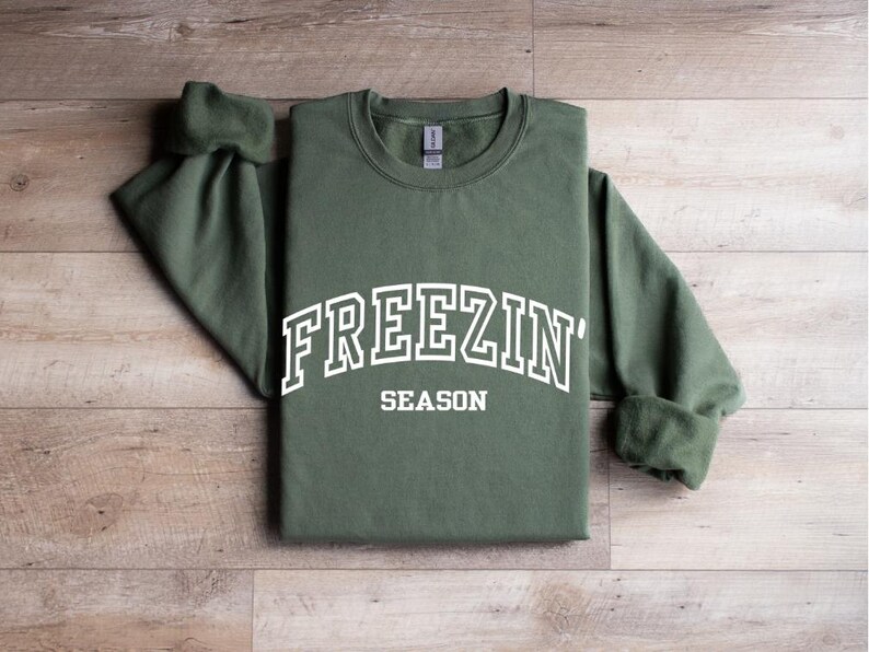 Może przedstawiać: Zielona bluza z białym napisem "Freezin' Season".