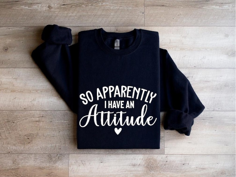 K&ouml;nnte beinhalten: Schwarzer Pullover mit wei&szlig;em Text, der "So Apparently I Have An Attitude" lautet, mit einem kleinen wei&szlig;en Herz unter dem Text.