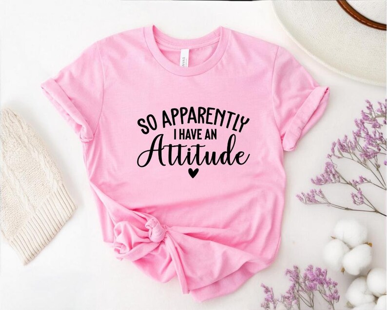 K&ouml;nnte beinhalten: Rosa T-Shirt mit schwarzem Text, der "So Apparently I Have An Attitude" mit einem kleinen schwarzen Herz lautet.