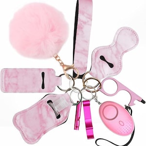 May include: A collection of pink marble-patterned keychain accessories, including a fluffy pom-pom, wrist strap, personal alarm, and bottle holder. The set also includes a bottle opener and a whistle, all attached to key rings.
