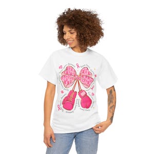 May include: White t-shirt with a pink ribbon bow and pink boxing gloves, with the words "Breast Cancer Awareness" in a circular pattern. The design includes pink ribbons and flowers.