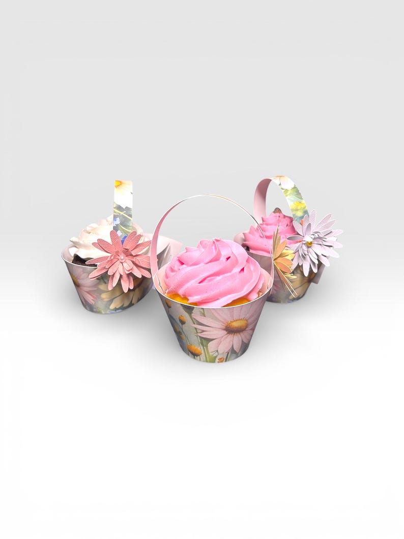 May include: Three cupcakes in decorative paper baskets. The baskets are adorned with a floral daisy pattern and feature pink frosting. Each cupcake is decorated with a paper flower and a handle, creating a charming presentation.
