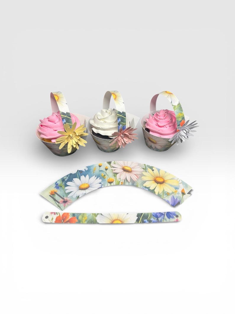 May include: Three cupcakes in decorative paper baskets with floral handles and flower accents. The cupcakes have pink and white frosting. Additional floral cupcake wrappers are also shown.