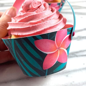 May include: Pink frosted cupcake in a teal and black cupcake wrapper with a pink flower design and a pink handle.