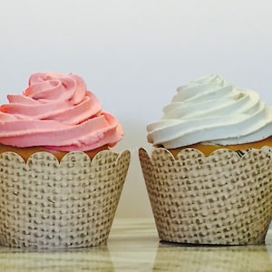 May include: Two cupcakes with brown burlap cupcake liners. One cupcake has pink frosting and the other has white frosting.