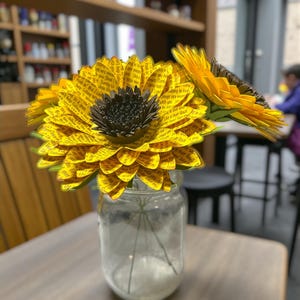 May include: A clear glass jar holds paper sunflowers with yellow petals and dark brown centers. The petals are printed with text. The text on the image reads: "Example of Smaller Center on a 4.5" Sun Flower."