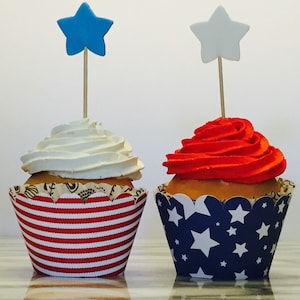 May include: Two cupcakes decorated with red and white frosting and topped with blue and white stars. The cupcakes are in red, white, and blue striped and blue and white star patterned cupcake liners.