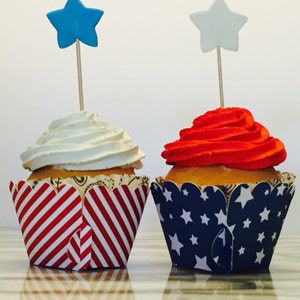May include: Two cupcakes decorated with red, white and blue frosting and star-shaped toppers. The cupcakes are in red and white striped and blue and white star-patterned cupcake wrappers.