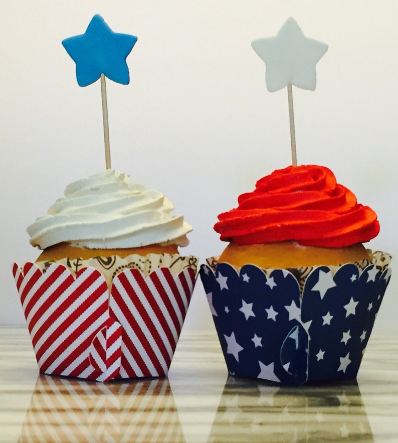 May include: Two cupcakes decorated with red, white and blue frosting and star-shaped toppers. The cupcakes are in red and white striped and blue and white star-patterned cupcake wrappers.
