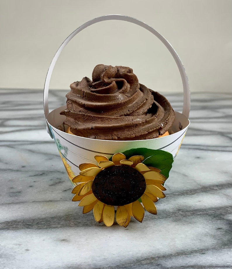 May include: A chocolate cupcake with a swirl of frosting in a white paper cupcake holder with a sunflower design and a handle.