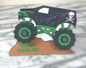 Może przedstawiać: Czarny i zielony monster truck z fioletowymi błyskawicami i wzorem czaszki i skrzyżowanych kości. Ciężarówka jedzie w górę brązowego wzgórza. Na wzgórzu nadrukowany jest tekst "Stellan's Monster Jam!"