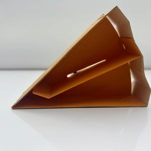 May include: A cardboard triangle-shaped box with a brown exterior and an orange interior. The box has a slot on the side and is designed to hold a single item.