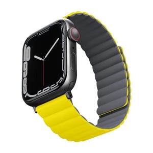 Op de afbeelding: Een zilveren smartwatch met een zwart scherm en een gele en grijze magnetische band. De wijzerplaat geeft de tijd weer. De band is gemaakt van een geribbeld, flexibel materiaal. De horloge heeft een rode knop aan de zijkant.