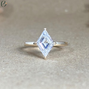 May include: A gold engagement ring with a kite-shaped, clear gemstone. The ring has a thin band and a four-prong setting. The word "engage" is visible on the ring.