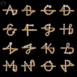 Könnte beinhalten: Eine Sammlung von sechzehn Goldringen, die jeweils als ein anderer Buchstabe des Alphabets von A bis P geformt sind. Jeder Ring besteht aus einem dünnen Goldband, das mit mehreren kleinen, runden, klaren weißen Steinen besetzt ist.