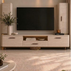 May include: A beige media console unit with a stone-like texture, featuring two tall side cabinets, a central drawer, and an open shelf. The furniture has dark brown leather-wrapped handles, gold-toned metal accents, and a flat-screen television mounted above.