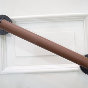 Puede incluir: Un tirador de puerta marrón y negro. El tirador tiene un agarre cilíndrico marrón y está montado en una puerta blanca. Los extremos del tirador son negros y tienen un diseño decorativo y redondeado.
