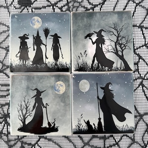 May include: A set of four square ceramic coasters featuring black silhouettes of witches against a night sky with a full moon. Each coaster displays a different scene, including witches with broomsticks, a raven, a cat, and bare trees.