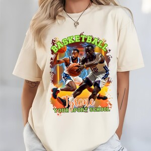 May include: Cream-colored t-shirt featuring a basketball-themed graphic. The design includes two basketball players in action, a basketball, and the words "BASKETBALL" and "Tyrone YOUR SPORT SCHOOL" in green and orange.