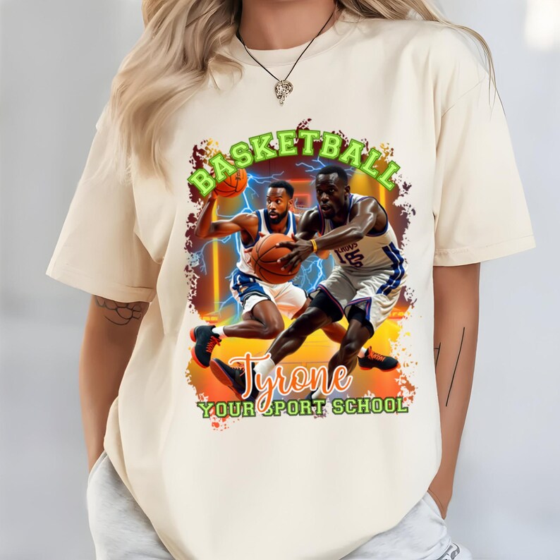 May include: Cream-colored t-shirt featuring a basketball-themed graphic. The design includes two basketball players in action, a basketball, and the words "BASKETBALL" and "Tyrone YOUR SPORT SCHOOL" in green and orange.