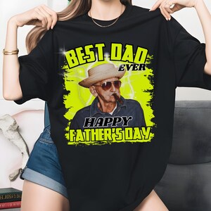 K&ouml;nnte beinhalten: Schwarzes T-Shirt mit einer Grafik eines Mannes mit Hut und Sonnenbrille, der eine Zigarre raucht. Der Text "BEST DAD EVER" und "HAPPY FATHER'S DAY" sind in Gr&uuml;n und Gelb. Der Hintergrund ist hellgelb mit Blitzdesigns.
