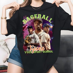 May include: Black t-shirt featuring a baseball-themed graphic. The design includes the word "BASEBALL" in green, and the name "Tyrone" with the text "YOUR SPORT SCHOOL". The graphic showcases three baseball players against a cosmic background.