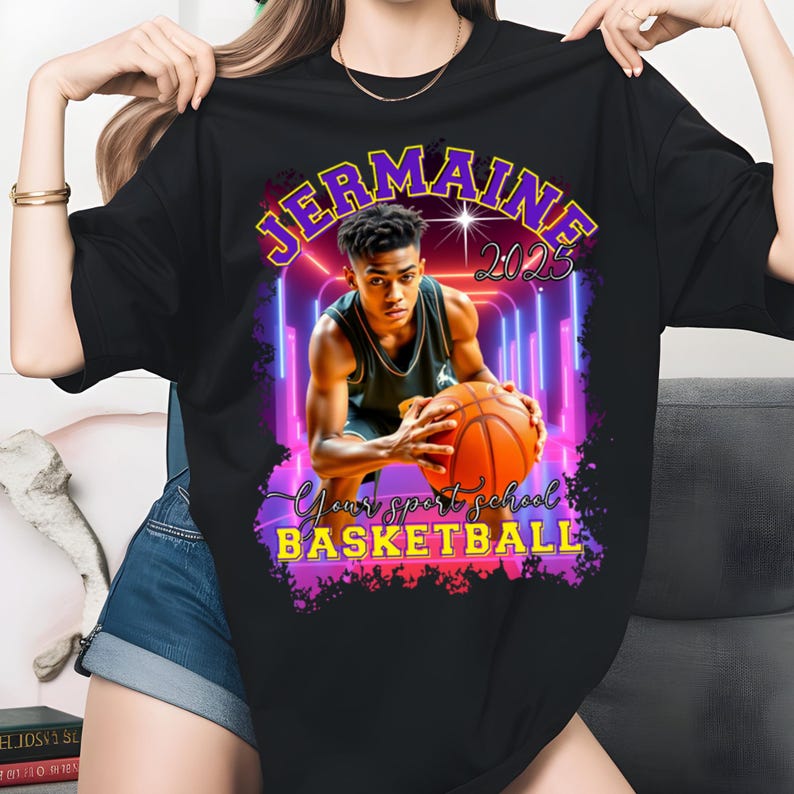 May include: Black t-shirt featuring a basketball player holding a basketball. The shirt has the name "Jermaine" and the year "2023" in a purple and yellow design. The text "Your sport school BASKETBALL" is also visible.