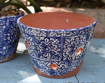 May include: Blue and white ceramic planter with a terracotta rim and drainage holes. The planter has a floral pattern.